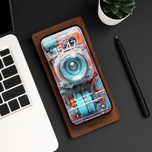 Puede incluir: Una funda de teléfono de cuero marrón con un teléfono transparente en su interior. La pantalla del teléfono muestra un reloj con la hora 15:47 y la fecha del lunes 22 de julio. El fondo del teléfono es un diseño azul y naranja de un dispositivo mecánico.