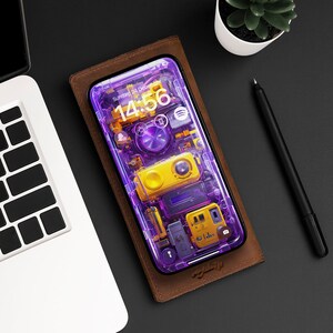 May include: A purple and yellow smartphone with a transparent back panel. The phone's screen displays a clock with the time 14:56 and the date Sunday 24 December. The phone is in a brown leather case.
