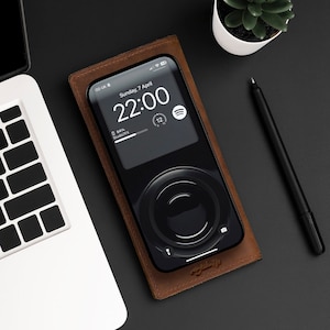 May include: A brown leather phone case with a black smartphone inside. The phone screen displays the time, "22:00", and the date, "Sunday, 7 April". The phone is 64% charged and is playing music from the Spotify app.