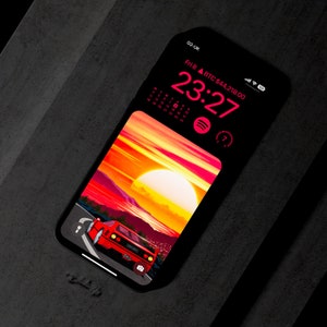 Peut inclure: Une voiture de sport rouge roule sur une route avec un coucher de soleil en arrière-plan. La voiture est une Ferrari avec un intérieur noir. L'écran du téléphone affiche une horloge numérique affichant 23:27, un calendrier et une icône de lecteur de musique.