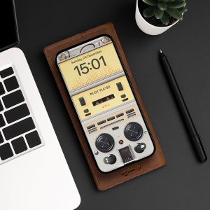 May include: A brown leather phone case with a white and yellow phone screen displaying a music player app. The screen shows the time "15:01" and the text "Sunday, 24 December". The music player app has a retro design with a cassette tape and buttons.