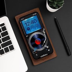 May include: A brown leather phone case with a built-in record player design. The phone screen displays a digital clock with the time 12:40 and the date Saturday, 10 February.
