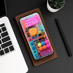 Pode incluir: Uma capa de telefone colorida com uma parte de trás transparente e uma variedade de botões e interruptores. A capa do telefone tem um relógio digital que mostra "Quarta-feira, 24 de julho 22:53".