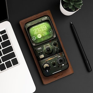 Könnte beinhalten: Eine braune Leder-Handyhülle mit einem grün-schwarzen Handydisplay, auf dem eine Digitaluhr mit der Zeit 21:19 und dem Text "Montag, 9. Oktober" angezeigt wird. Der Handybildschirm zeigt auch ein stilisiertes Bild eines Vintage-Radios mit Zifferblättern und Knöpfen.