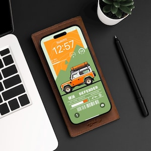 Può includere: Una custodia per telefono in pelle marrone con uno schermo del telefono verde e arancione che mostra un orologio digitale e un'immagine di un fuoristrada verde con il testo "DEFENDER" e "OFF-ROAD VEHICLE ADVENTURE".