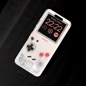 May include: A white phone case with a clear back and a Game Boy design. The case features a black and white Game Boy screen with a digital clock displaying "22:22" and the text "Sunday, 3 March". The case also has red buttons and a black directional pad.