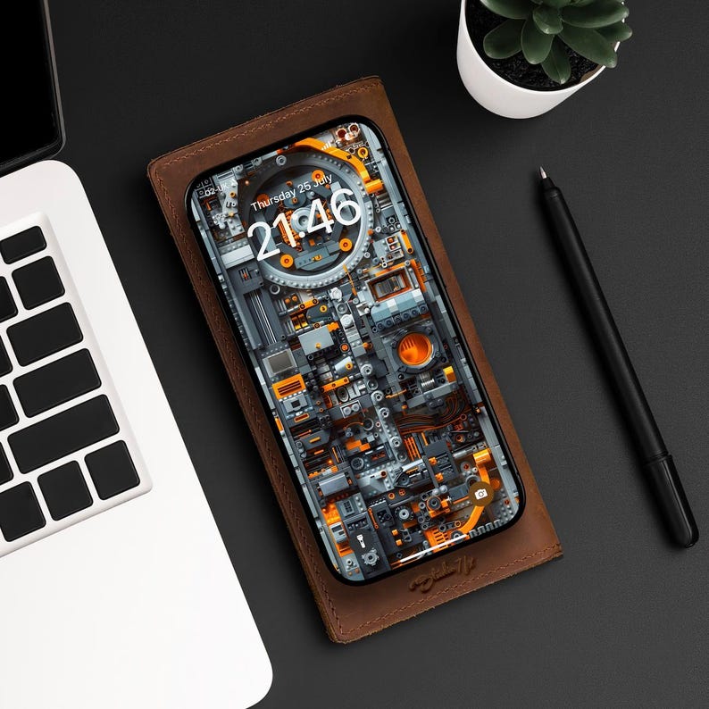 Pu&ograve; includere: Una custodia per telefono in pelle marrone con un iPhone nero all'interno. Lo schermo del telefono mostra un orologio digitale con l'ora 21:46 e la data gioved&igrave; 26 luglio. Lo sfondo del telefono &egrave; un design astratto colorato di ingranaggi e macchinari.