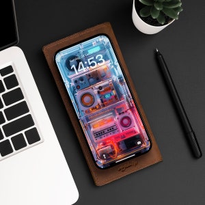 Puede incluir: Una funda de teléfono de cuero marrón con una parte posterior transparente que muestra una pantalla de teléfono con un reloj digital que muestra "Domingo, 24 de diciembre 14:53" y un diseño abstracto colorido.