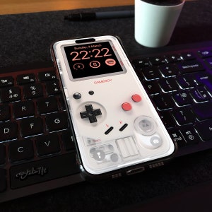 May include: A white phone case featuring a Game Boy design. The case has a black screen displaying the date and time: Sunday, 3 March 22:22. The case also includes a red and white Game Boy controller design with the words "GAMEBOY" printed on the case.
