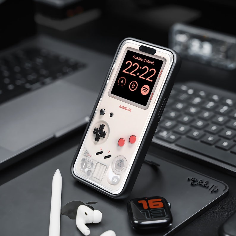 May include: A white and black phone case with a Game Boy design. The case has a clear screen that shows a digital clock displaying "22:22" and the date "Sunday, 3 March". The case also has a red and white Game Boy controller design.
