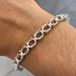 Puede incluir: Una pulsera de metal plateado que presenta una serie de engastes ovalados vacíos. Cada engaste está diseñado con cuatro pequeñas garras destinadas a sujetar una piedra preciosa, conectadas por una estructura de cadena flexible alrededor.