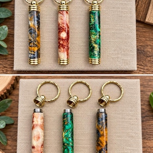 May include: Three cylindrical keychains with gold-tone metal hardware and marbled resin bodies in amber, red, and green. The top section of each keychain unscrews to reveal a hollow interior, allowing the metal ring to be detached from the body.