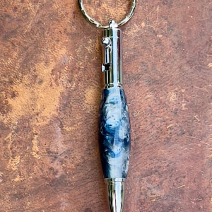 May include: A silver pen with a blue and white swirl pattern, attached to a silver key ring.