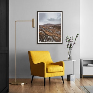 K&ouml;nnte beinhalten: Ein modernes Wohnzimmer mit einem gerahmten Landschaftsfoto, einem gelben Sessel und einer goldenen Stehlampe. Das Foto zeigt eine Berglandschaft unter einem bew&ouml;lkten Himmel. Ein kleiner Beistelltisch tr&auml;gt eine Vase mit Blumen.