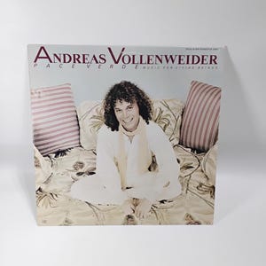 May include: A vinyl record cover featuring Andreas Vollenweider, Pace Verde Music for Living Beings. The cover shows a person with curly hair wearing a white shirt and scarf, sitting on a patterned cushion between two striped pillows.