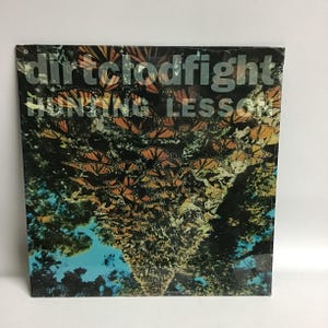 May include: A vinyl record album cover with a black background and the text "dirt clodfight" and "hunting lesson" in white. The background image is a close-up of a tree with a large number of orange and black butterflies.