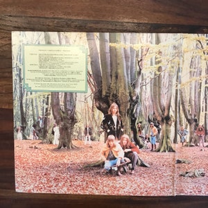 May include: A vintage vinyl record album cover featuring a band of three men standing in a forest. The album is titled "Trilogy" by Emerson, Lake & Palmer. The album cover is a psychedelic image with a green and yellow color scheme.