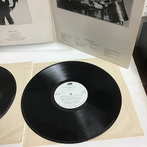 K&ouml;nnte beinhalten: Eine schwarze Schallplatte mit einem wei&szlig;en Label. Das Label tr&auml;gt den Text "Emerson, Lake & Palmer" und "Greg Lake". Die Schallplatte liegt auf einer wei&szlig;en Papieroberfl&auml;che.