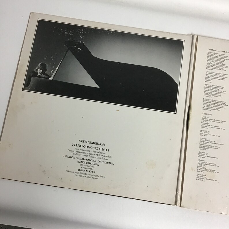 K&ouml;nnte beinhalten: Ein Schwarzwei&szlig;foto einer Person, die Klavier spielt. Der Text auf der R&uuml;ckseite des Schallplattenalbums lautet "Keith Emerson Piano Concerto No. 1" und "London Philharmonic Orchestra".