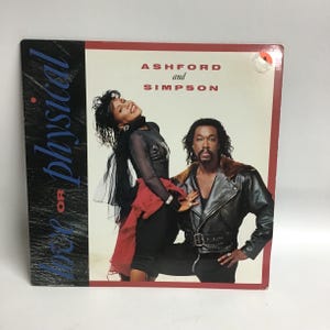 May include: A vinyl record cover featuring Ashford and Simpson. The cover is red and white with a photo of the duo in black and white. The text "Ashford and Simpson" is in black and the text "Is It Still Good To Ya" is in white.