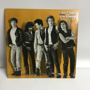 May include: A yellow vinyl record album cover featuring a band called Tommy Conwell and the Young Rumblers. The band members are wearing leather jackets, jeans, and t-shirts. The album title is "Rumble" and is printed in white letters.