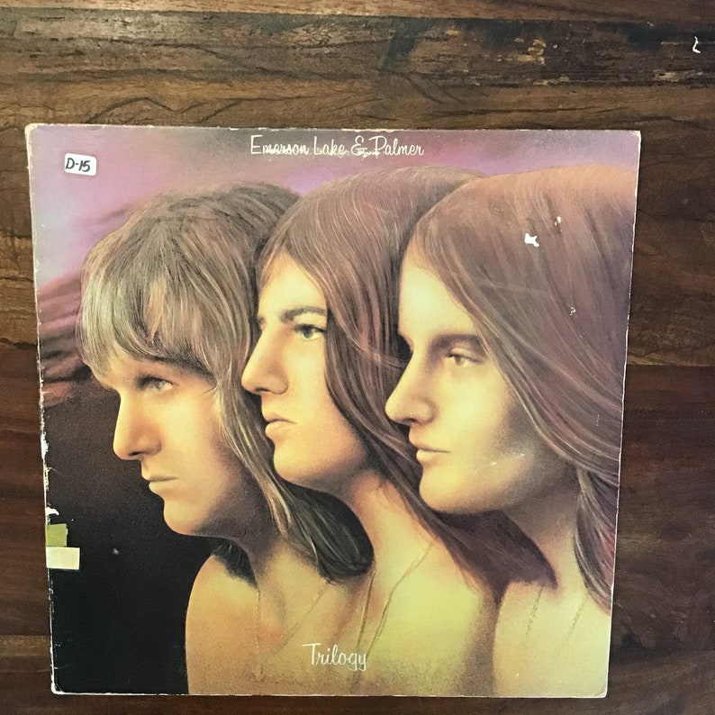 May include: A vintage vinyl record album cover featuring a photo of three men with long hair. The album is titled "Trilogy" by Emerson, Lake & Palmer.