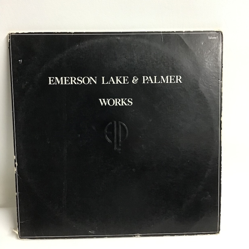 K&ouml;nnte beinhalten: Schwarzes Vinyl-Plattencover mit wei&szlig;em Text, der "Emerson Lake & Palmer" und "Works" lautet. Das Albumcover zeigt auch ein wei&szlig;es "ELP"-Logo.