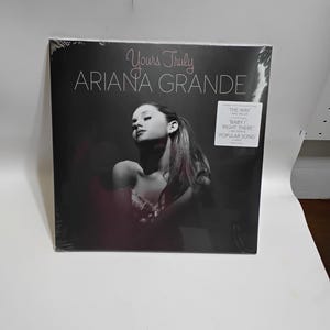 May include: Sealed vinyl record of Ariana Grande's album "Yours Truly." The album cover features a black and white image of Ariana Grande. The album title and artist name are in white text. A sticker on the front lists popular songs.