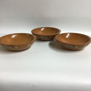 May include: Set of three wooden bowls with a brown glaze and painted designs of stylized animals. The bowls are small and perfect for serving snacks or dips.