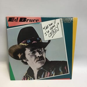May include: Album cover for Ed Bruce's "Tell 'em I've Gone Crazy." The album art features a portrait of a man wearing a cowboy hat. The album cover has a color scheme of pink, teal, yellow, and gray.
