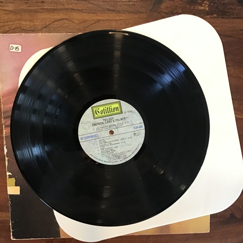 May include: Black vinyl record with a white label. The label has the text "Cotillion" in yellow, "Trilogy" in black, "Emerson, Lake & Palmer" in black, and "SD 9942" in black. The label also has the text "Stereo" in white and "One" in white.