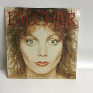 May include: A vinyl record album cover featuring a close-up portrait of Cheryl Dilcher. The album title "Blue Sailor" is printed in white letters at the bottom of the cover.