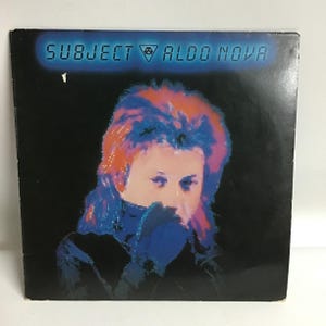 May include: A black vinyl record album cover with the title "SUBJECT ALDO NOVA" in white text. The cover features a colorful image of a person with pink and blue hair, wearing a black jacket and looking down.