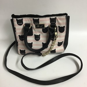 Può includere: Una borsa a mano a righe bianche e rosa con facce di gatti neri e una tracolla a catena dorata. La borsa ha un manico superiore e una tracolla rimovibile.