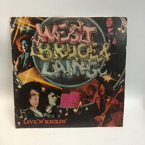 May include: Vintage vinyl record album cover for "West, Bruce & Laing - Live 'N' Kickin'". The cover features a colorful design with band members' images, musical notes, and the band's name in a stylized font. The album cover is slightly worn.