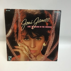 May include: A vintage vinyl record cover featuring Joni James. The cover is a close-up of Joni James, with a background of a beaded curtain. The text on the cover reads "Joni James" and "Like 3 O'Clock In The Morning".