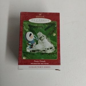 May include: A Hallmark Keepsake Ornament featuring a frosted scene with a person in a blue parka and a polar bear. The ornament is part of the Collector's Series and is titled "Frosty Friends".