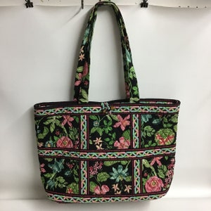 Puede incluir: Un bolso tote acolchado negro con un estampado floral en tonos rosa, verde y azul. El bolso tiene dos asas largas y una cremallera.