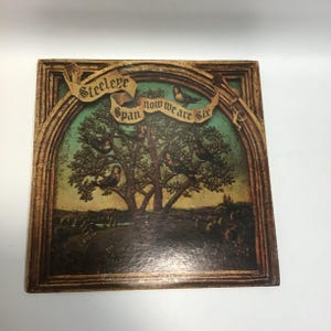 May include: A vintage vinyl record album cover featuring a green and brown illustration of a tree with birds and a castle in the background. The album title "Steeleye Span Now We Are Six" is written in a banner across the top of the image.