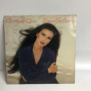 May include: A vinyl record album cover featuring a woman with long dark hair, wearing a blue shirt. The album title is "Women Get Lonely" by "Charly McClain".