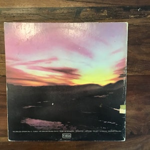 May include: Back cover of a vinyl record with a sunset scene. The record is titled "The Endless Enigma" and includes the song titles "Fugue", "From The Beginning", "The Sheriff", "Hoedown", "Trilogy", "Living Sin", and "Abaddon's Bolero".