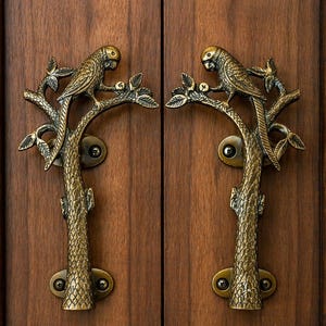 May include: Two brass door handles with a parrot perched on a branch design. The handles are mounted on a dark brown wooden door. The parrot and branch details are intricately crafted, adding a touch of nature-inspired elegance to the door.