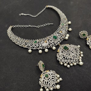 May include: A silver and white necklace with green gemstones and pearl accents. The necklace is paired with matching earrings.