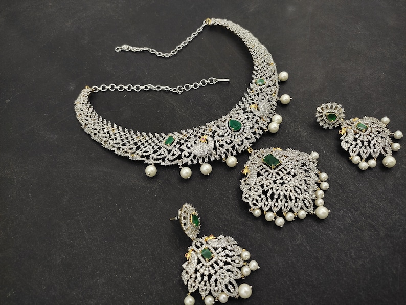 May include: A silver and white necklace with green gemstones and pearl accents. The necklace is paired with matching earrings.