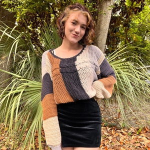 May include: A woman wearing a brown, black and white striped crocheted jumper with a black velvet skirt.