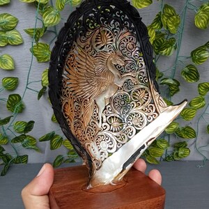 This is a real and natural mother of pearl shell polished and hand carved with wooden stand by a very skilled carving artist in his field. It is very detailed with pegasus design and has high artistic value