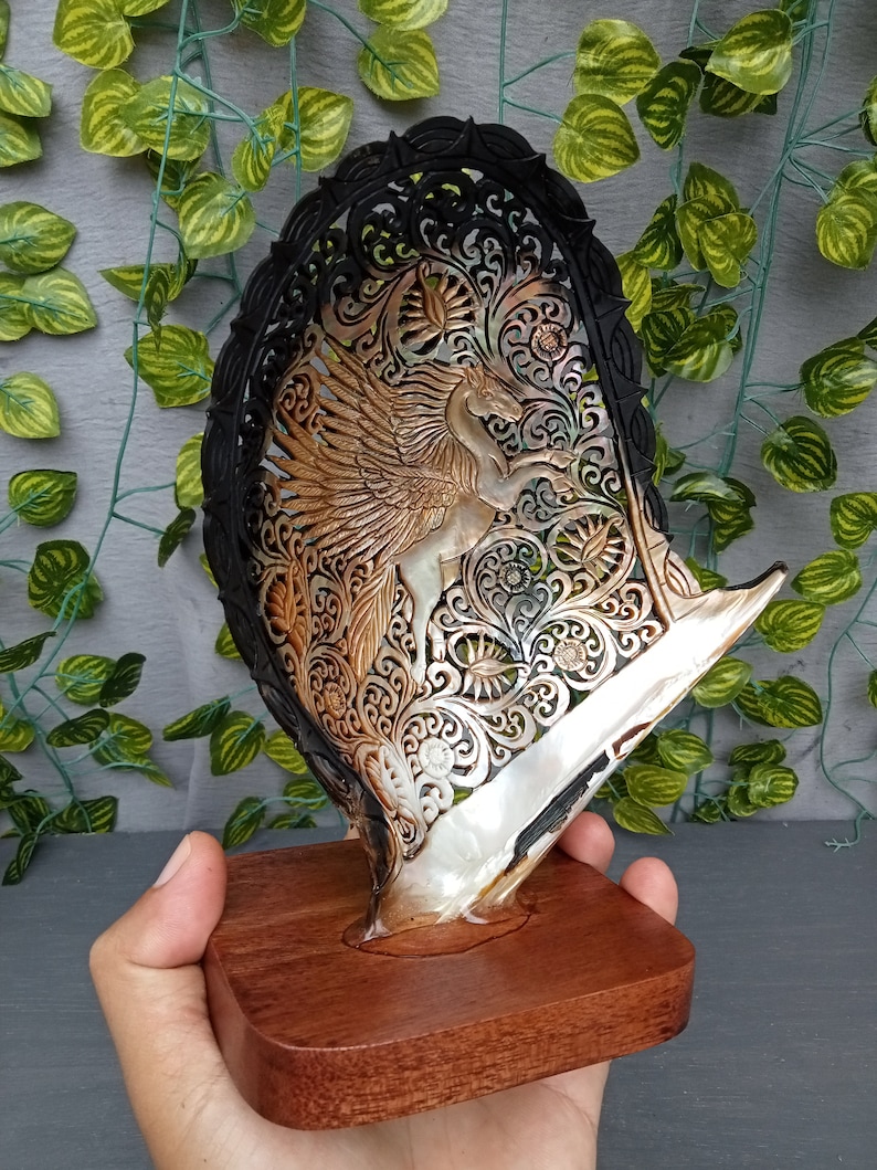 This is a real and natural mother of pearl shell polished and hand carved with wooden stand by a very skilled carving artist in his field. It is very detailed with pegasus design and has high artistic value