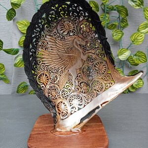 This is a real and natural mother of pearl shell polished and hand carved with wooden stand by a very skilled carving artist in his field. It is very detailed with pegasus design and has high artistic value