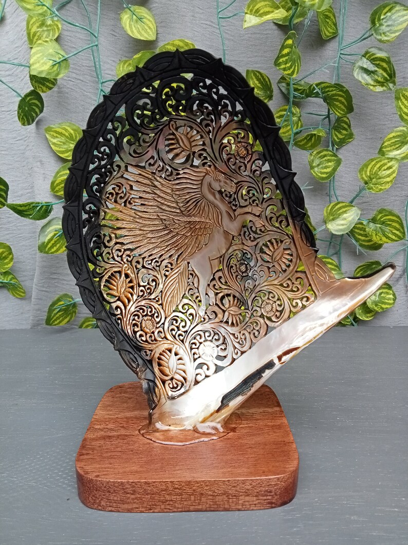 This is a real and natural mother of pearl shell polished and hand carved with wooden stand by a very skilled carving artist in his field. It is very detailed with pegasus design and has high artistic value