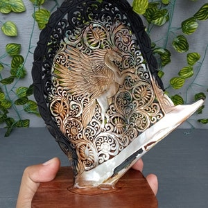 This is a real and natural mother of pearl shell polished and hand carved with wooden stand by a very skilled carving artist in his field. It is very detailed with pegasus design and has high artistic value